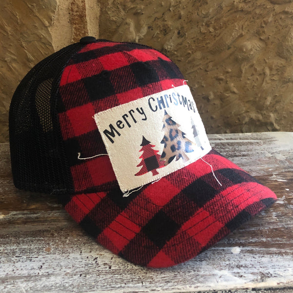 Red and black checkered cap with 'Merry Christmas' patch on a wooden surface