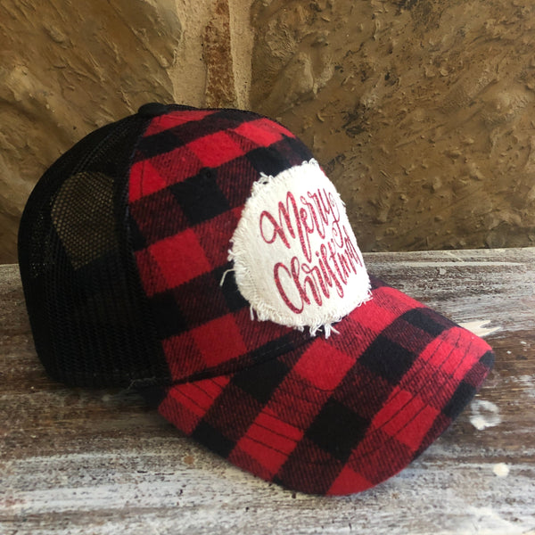 Red and black plaid cap with 'Merry Christmas' text on a wooden surface.