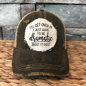 Distressed brown cap with a white patch featuring dramatic text placed on a woven surface with a stone wall background.